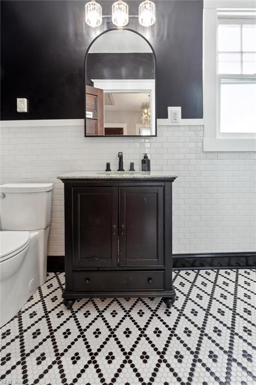 half bathroom with tile patterned floors, wainscoting, vanity, tile walls, and toilet