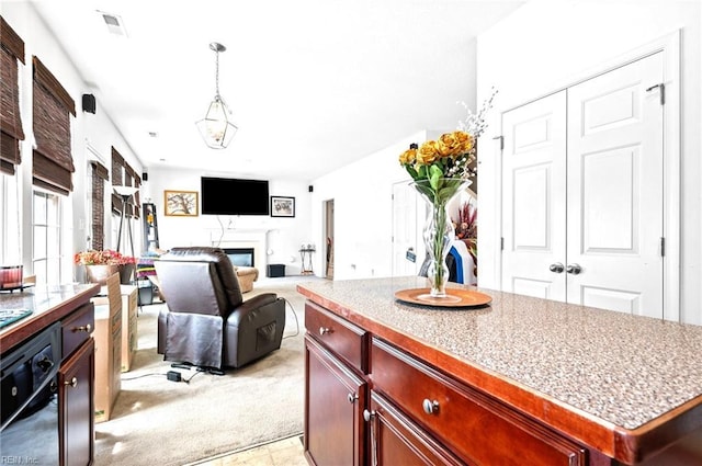 kitchen featuring dark brown cabinets, decorative light fixtures, a center island, a glass covered fireplace, and light colored carpet