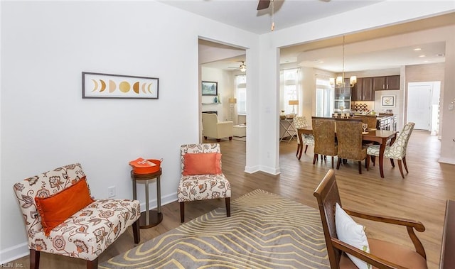 sitting room with baseboards, ceiling fan with notable chandelier, and wood finished floors