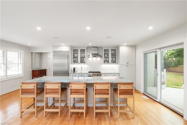 kitchen with wall chimney range hood, built in refrigerator, tasteful backsplash, range, and a healthy amount of sunlight