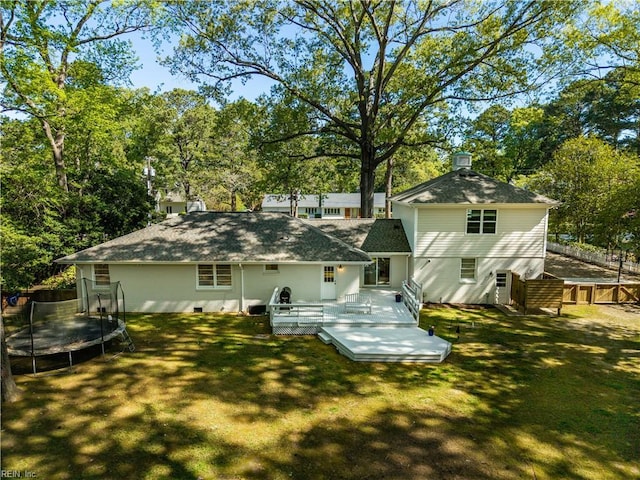 back of house with a lawn, fence, a deck, and a trampoline