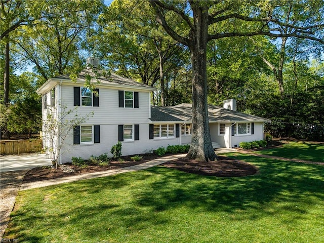 view of front of property with fence, a chimney, brick siding, and a front lawn