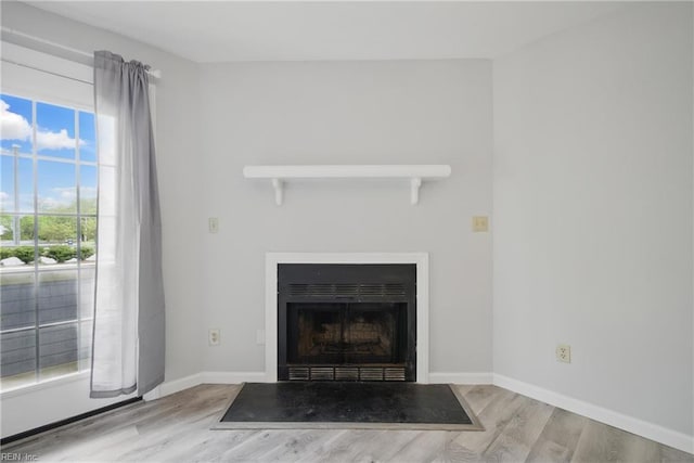 interior details with a fireplace with flush hearth, wood finished floors, and baseboards
