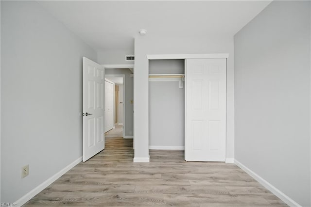 unfurnished bedroom with a closet, visible vents, wood finished floors, and baseboards