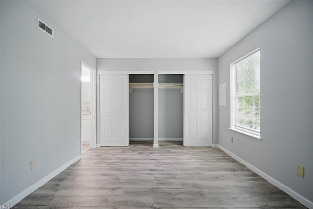 unfurnished bedroom with wood finished floors, visible vents, multiple closets, and baseboards