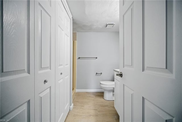 bathroom featuring wood finished floors, a closet, toilet, baseboards, and visible vents