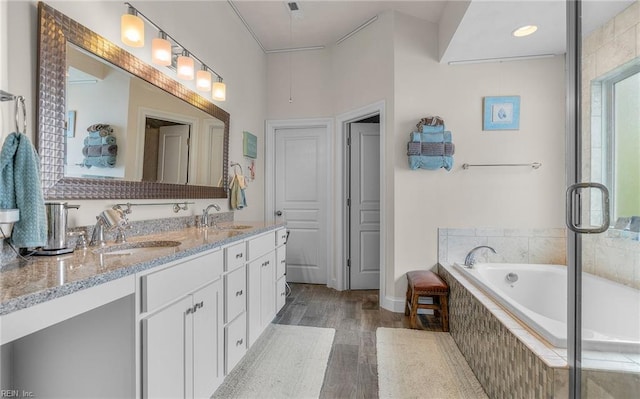 bathroom with double vanity, wood finished floors, a garden tub, and a sink