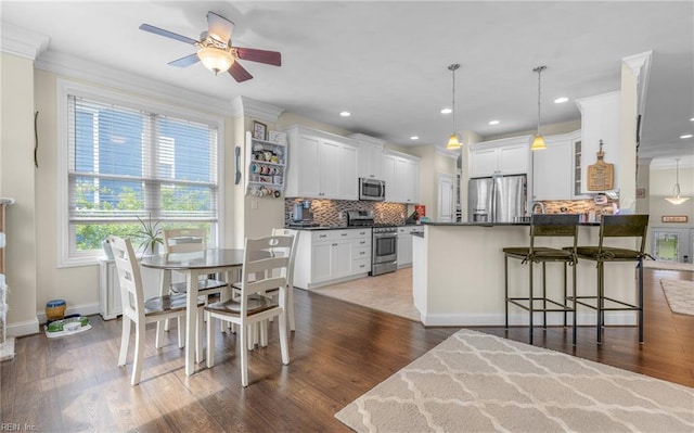 kitchen with a peninsula, a kitchen breakfast bar, dark countertops, decorative backsplash, and appliances with stainless steel finishes