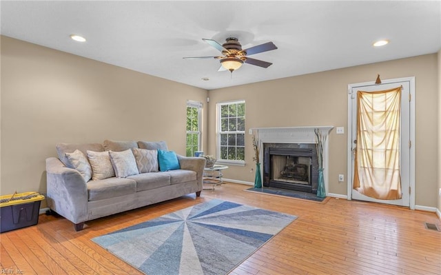 living area with a premium fireplace, ceiling fan, visible vents, baseboards, and hardwood / wood-style flooring
