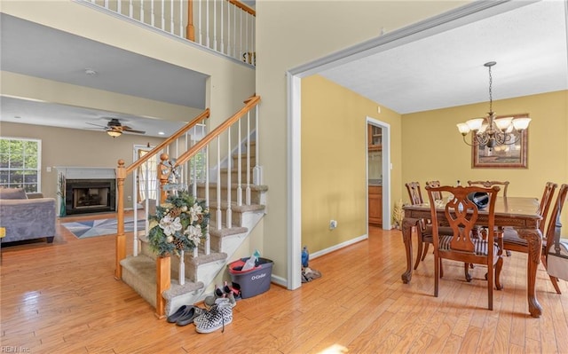 dining area with hardwood / wood-style flooring, ceiling fan with notable chandelier, stairs, and a fireplace