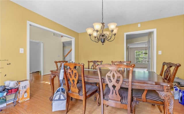 dining room featuring light wood finished floors, a notable chandelier, and stairway