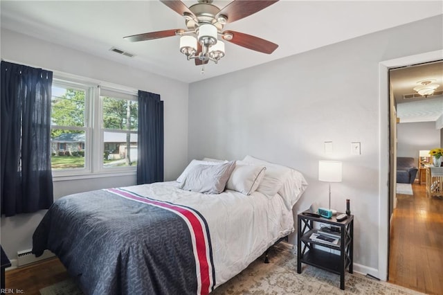 bedroom featuring baseboard heating, ceiling fan, wood finished floors, and visible vents