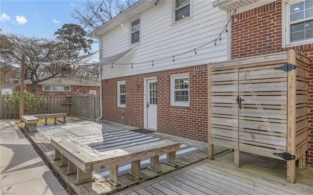 rear view of house featuring a wooden deck, brick siding, and fence