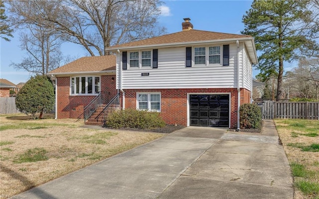 tri-level home with driveway, a chimney, fence, brick siding, and a garage