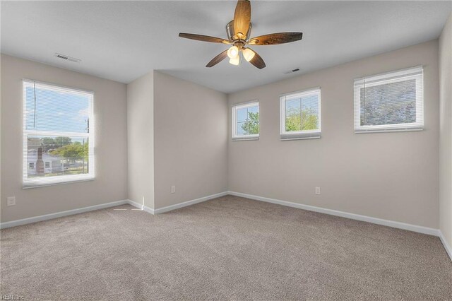 carpeted spare room with visible vents, a ceiling fan, and baseboards