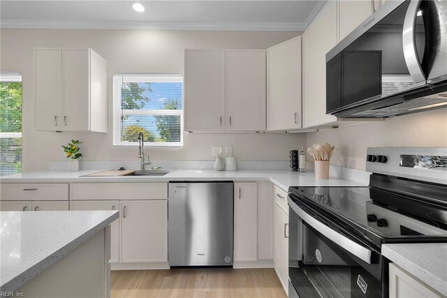 kitchen featuring crown molding, a sink, light wood-type flooring, white cabinets, and appliances with stainless steel finishes