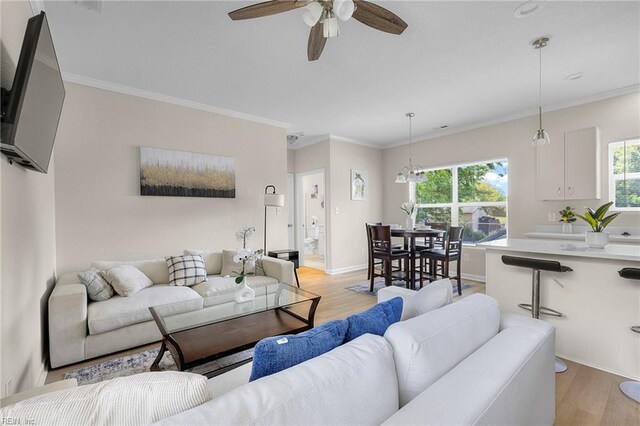 living room with light wood-style flooring, ornamental molding, and a ceiling fan