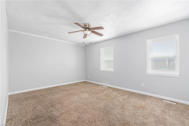 carpeted spare room featuring baseboards, visible vents, a ceiling fan, and crown molding