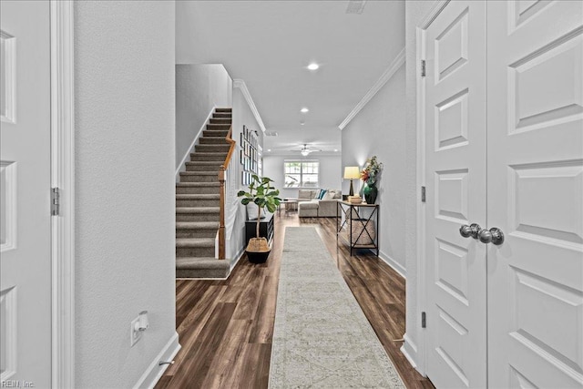 corridor with dark wood-style flooring, stairway, baseboards, ornamental molding, and a textured wall