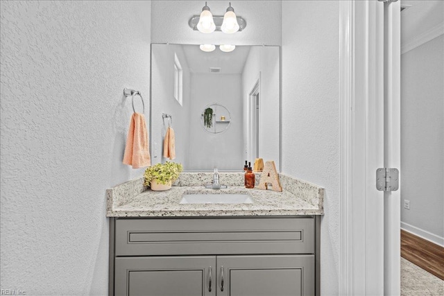 bathroom featuring vanity, a textured wall, baseboards, and wood finished floors