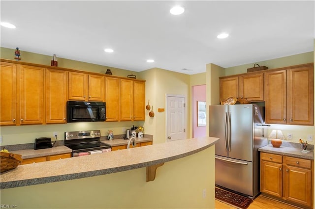 kitchen featuring brown cabinets, recessed lighting, appliances with stainless steel finishes, and a breakfast bar area
