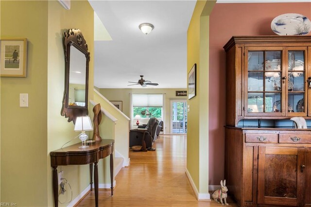 corridor with baseboards, light wood-style flooring, arched walkways, and stairs