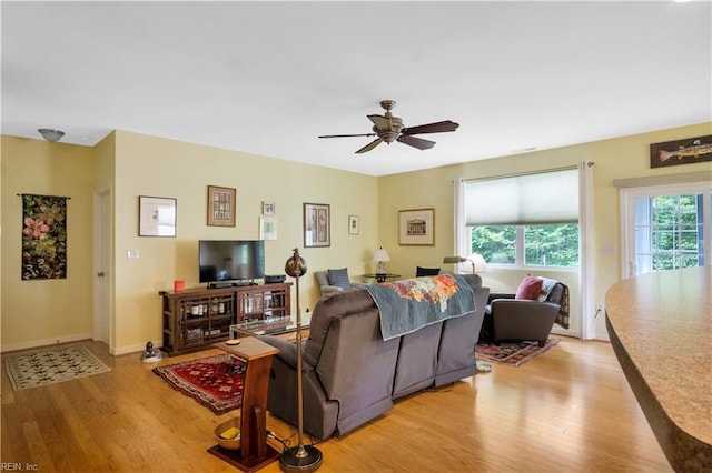living room featuring ceiling fan, baseboards, and light wood-style floors