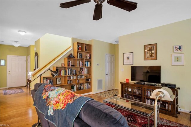 living area featuring baseboards, visible vents, a ceiling fan, wood finished floors, and stairway