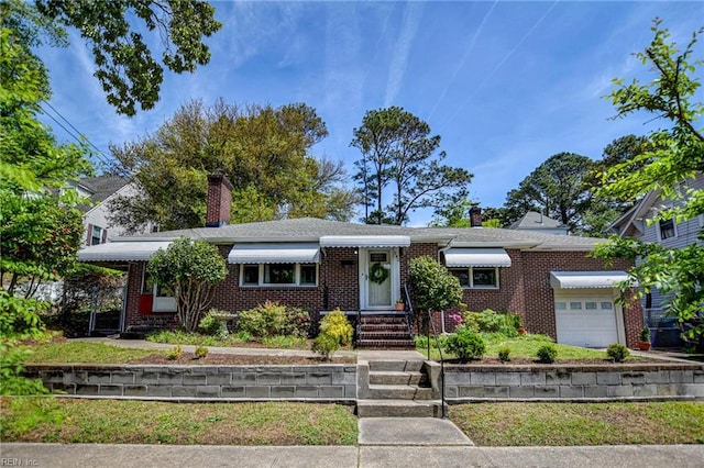 single story home featuring a chimney, an attached garage, and brick siding