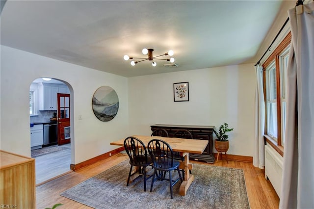dining space featuring a healthy amount of sunlight, light wood-type flooring, arched walkways, and an inviting chandelier