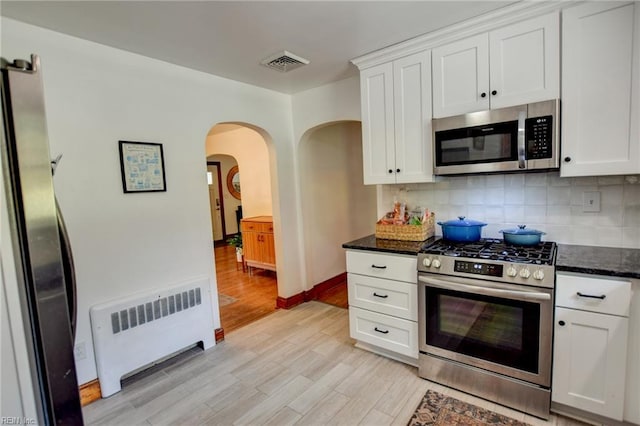 kitchen with light wood-style flooring, visible vents, stainless steel appliances, arched walkways, and radiator heating unit