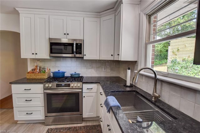 kitchen with dark stone counters, a sink, stainless steel appliances, light wood-style flooring, and white cabinets