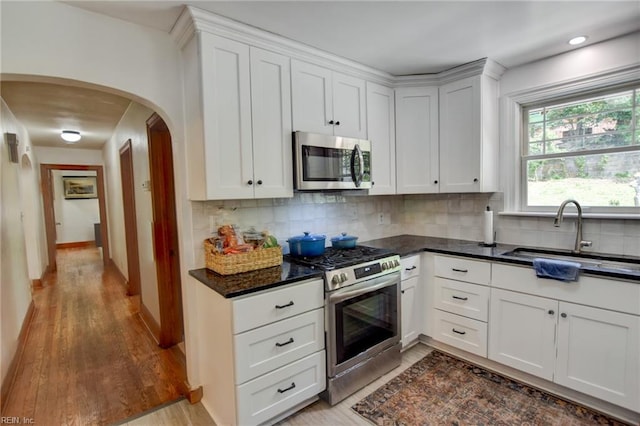 kitchen featuring arched walkways, light wood-style flooring, decorative backsplash, stainless steel appliances, and a sink