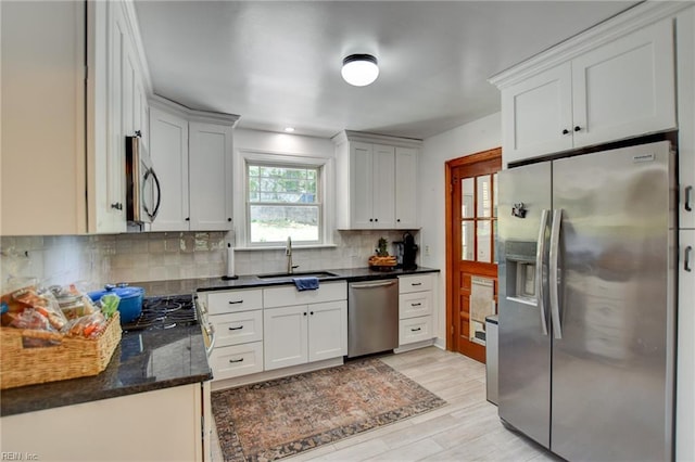 kitchen with a sink, tasteful backsplash, light wood-type flooring, white cabinets, and appliances with stainless steel finishes