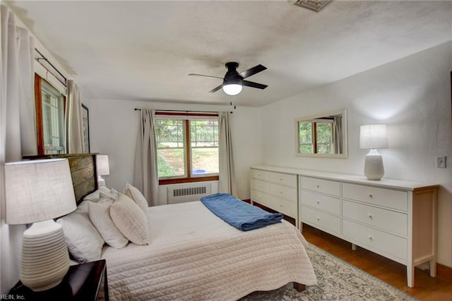 bedroom with visible vents, radiator heating unit, wood finished floors, and ceiling fan