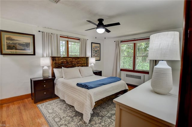 bedroom featuring radiator, multiple windows, light wood-style floors, and baseboards