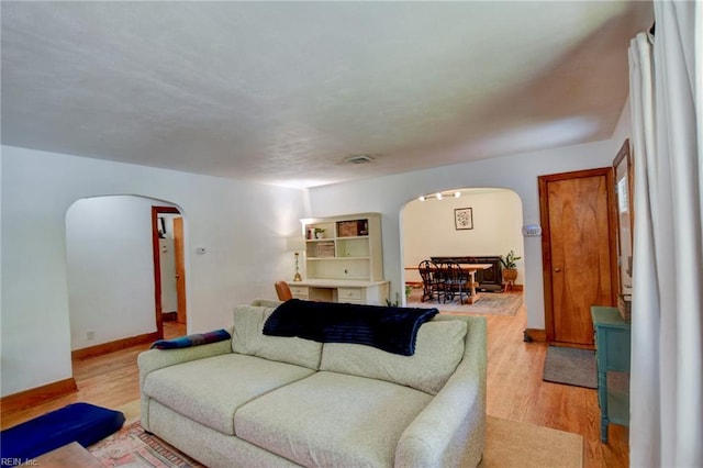 living room featuring baseboards, light wood-style flooring, and arched walkways