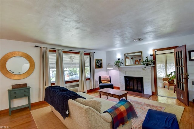 living room featuring a brick fireplace, visible vents, wood finished floors, and baseboards