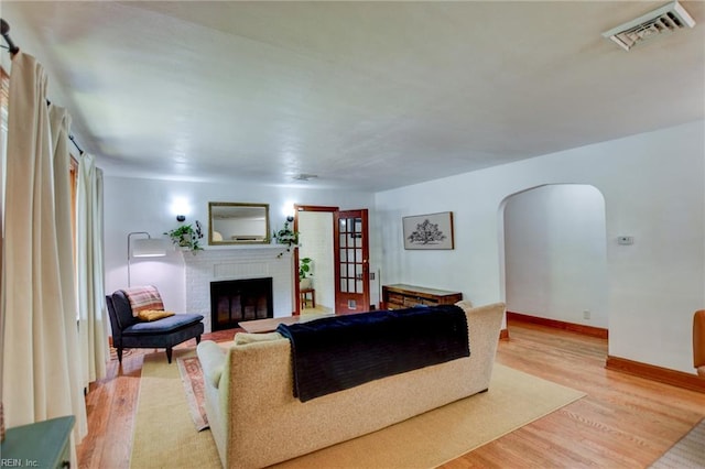 living room with visible vents, baseboards, arched walkways, light wood finished floors, and a fireplace