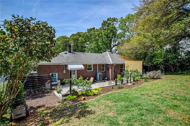 rear view of property with central air condition unit, a yard, a chimney, and brick siding