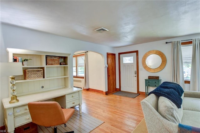 living room featuring a wealth of natural light, visible vents, light wood-style flooring, and arched walkways