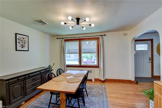 dining room with arched walkways, light wood-style floors, baseboards, visible vents, and a notable chandelier