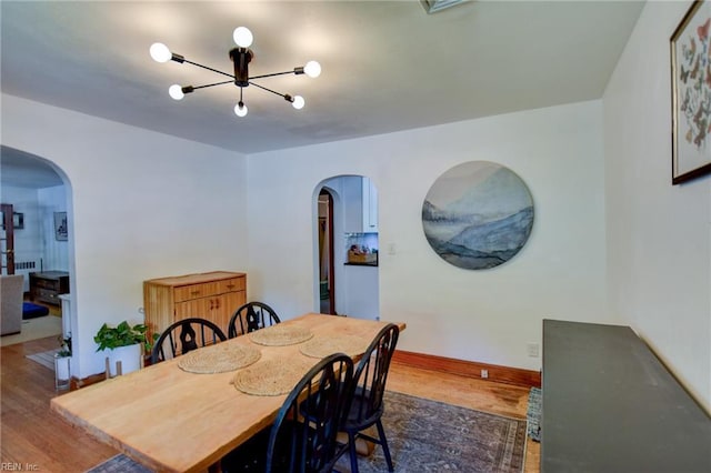 dining space with dark wood-style floors, baseboards, arched walkways, and a notable chandelier
