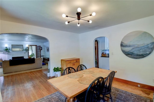 dining space with a chandelier, arched walkways, wood finished floors, and a fireplace
