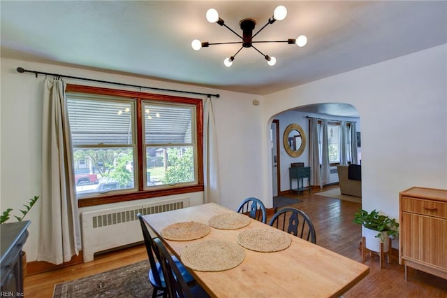 dining space with a chandelier, radiator heating unit, arched walkways, and wood finished floors
