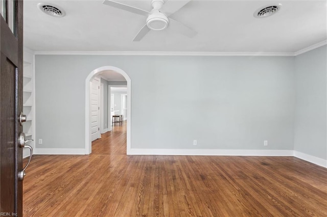 unfurnished room with a ceiling fan, baseboards, ornamental molding, arched walkways, and wood finished floors