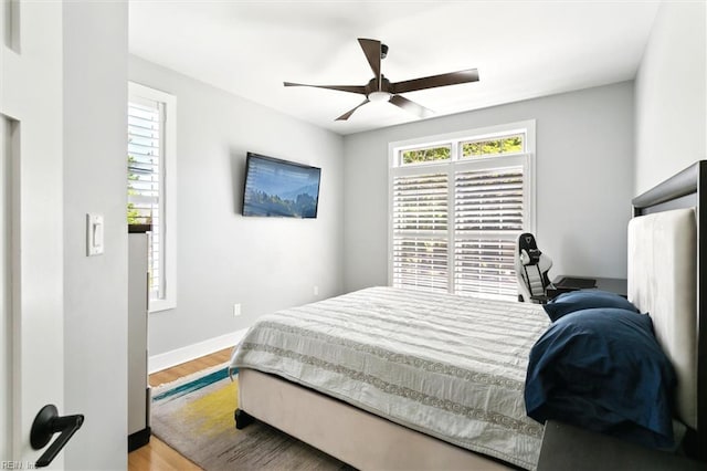 bedroom featuring ceiling fan, baseboards, multiple windows, and wood finished floors