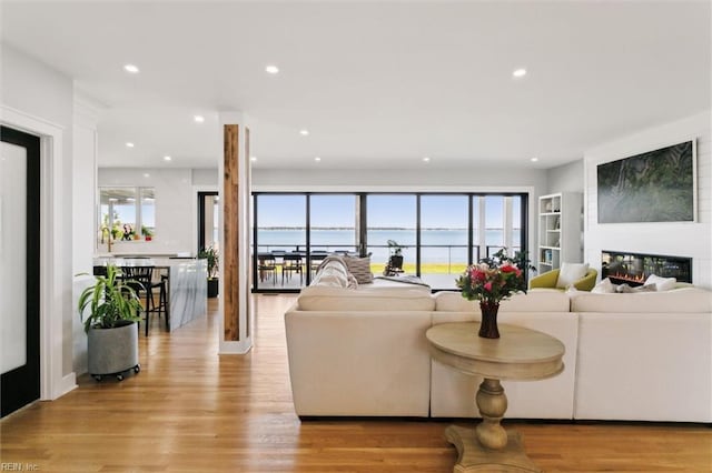 living room with light wood-style floors, a water view, a glass covered fireplace, and recessed lighting
