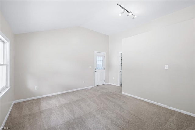 spare room featuring baseboards, vaulted ceiling, carpet flooring, and track lighting