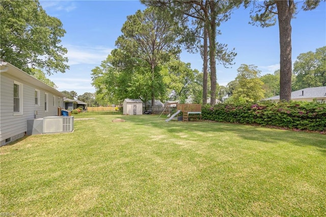 view of yard featuring central AC unit, a shed, a playground, fence, and an outbuilding